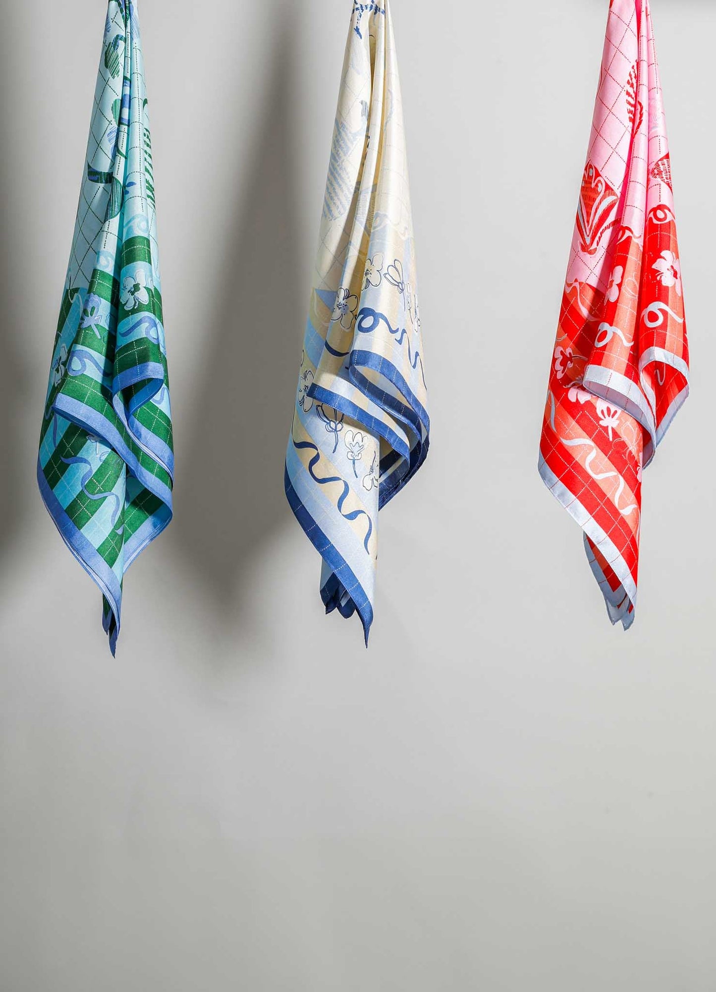 Set of three printed cotton tea towels with colorful floral and geometric patterns in blue, green, cream, and red tones, hanging against a plain background.