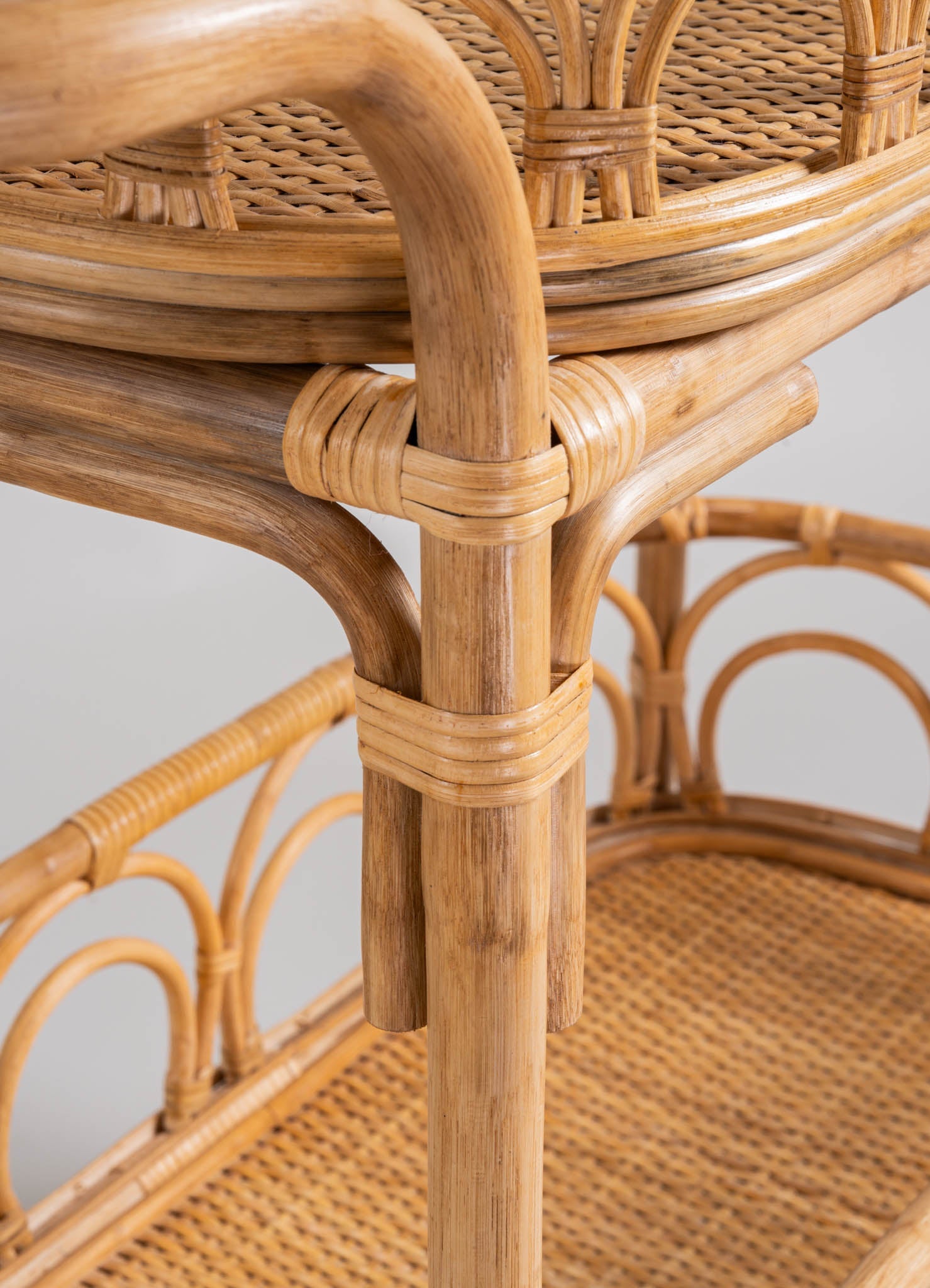 Rattan side table with a woven cane top, featuring curved legs and structural joints wrapped with rattan strips, in a natural wood finish.