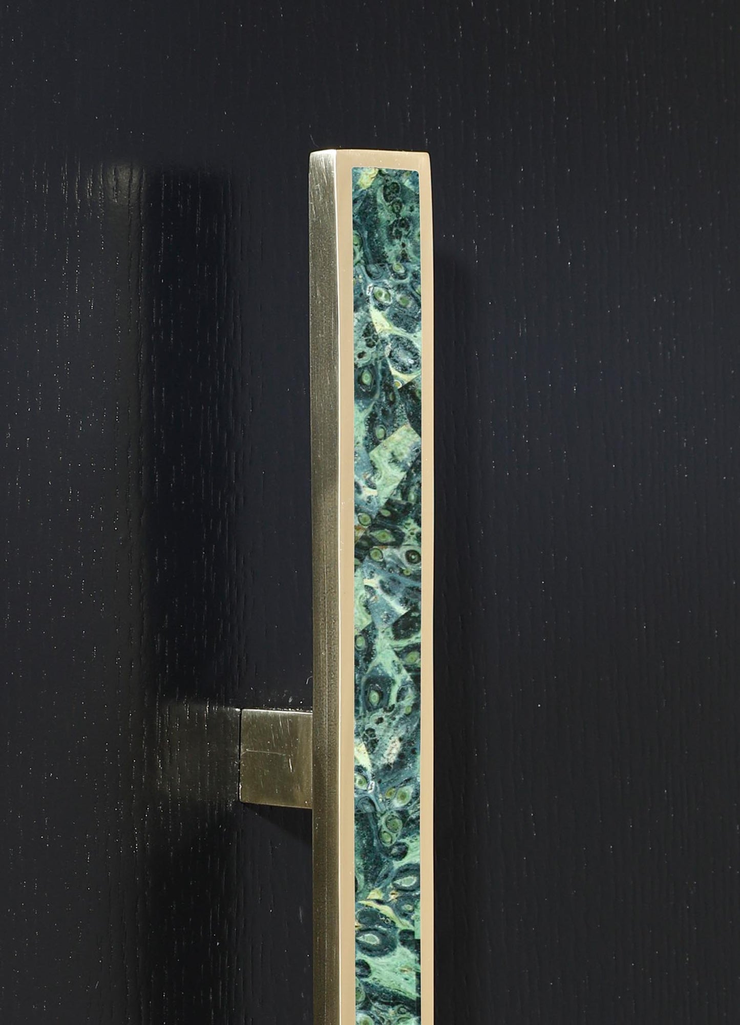 A vertical brass picture frame with a decorative inlay featuring an abstract pattern in shades of green, blue, and white. The frame has a contemporary style with a sleek metallic finish and is mounted on a black background.