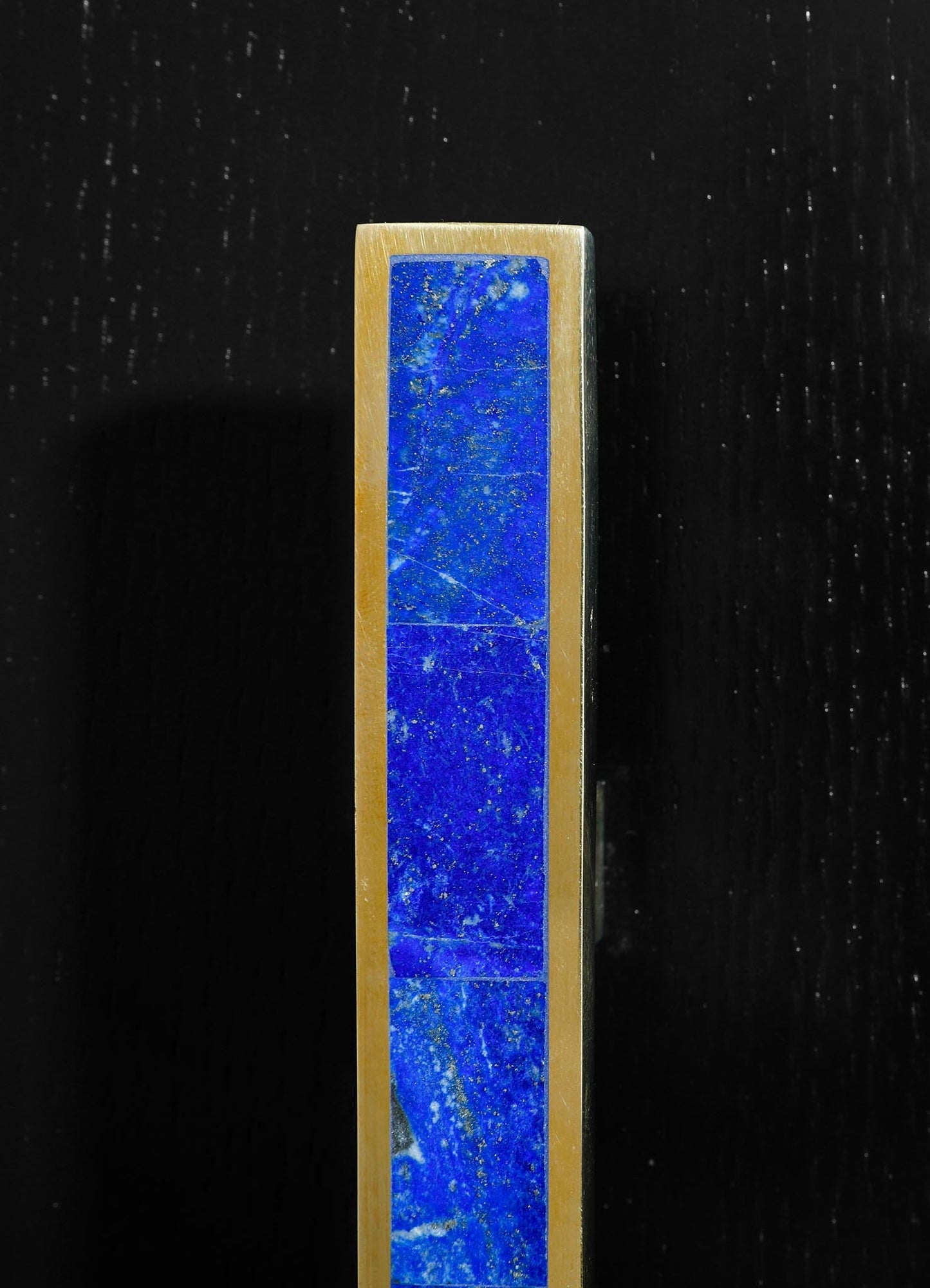 A tall, rectangular incense holder featuring a blue stone inlay with gold accents, made of brass or metal with a polished finish, set against a black background.