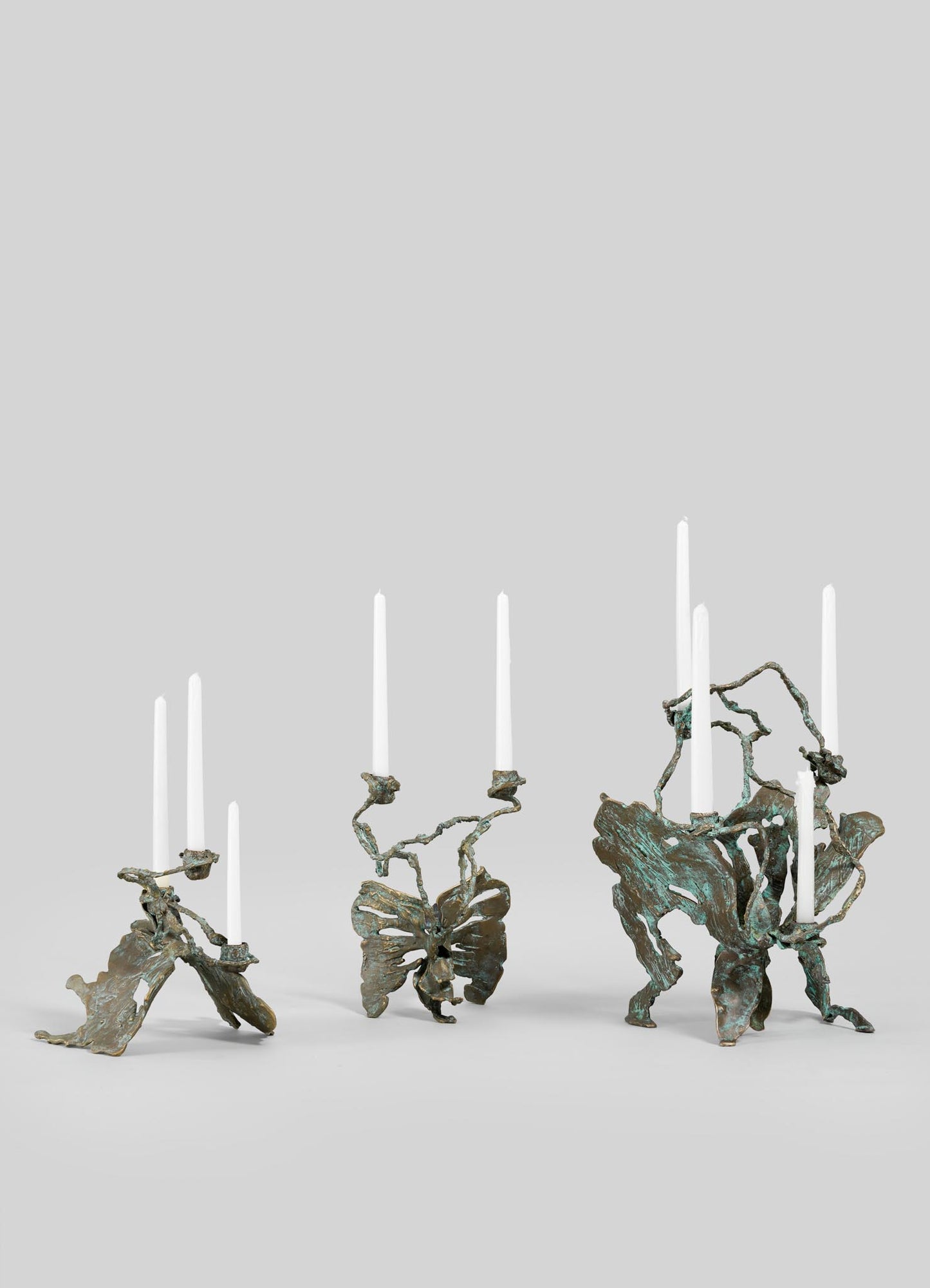 The VIYA Butterfly Candle Stand Large features an abstract, sculptural bronze design with organic, twisted forms, each holding two or three tall white taper candles. Displayed against a plain light gray background.
