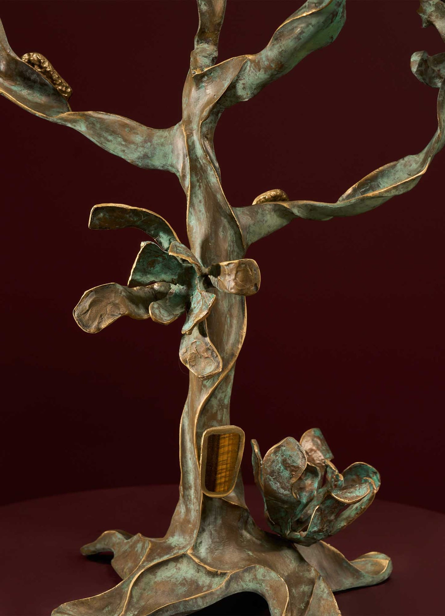 Bronze sculpture of a botanical motif with detailed leaves and a textured surface, featuring hints of green patina and gold accents against a dark red background.