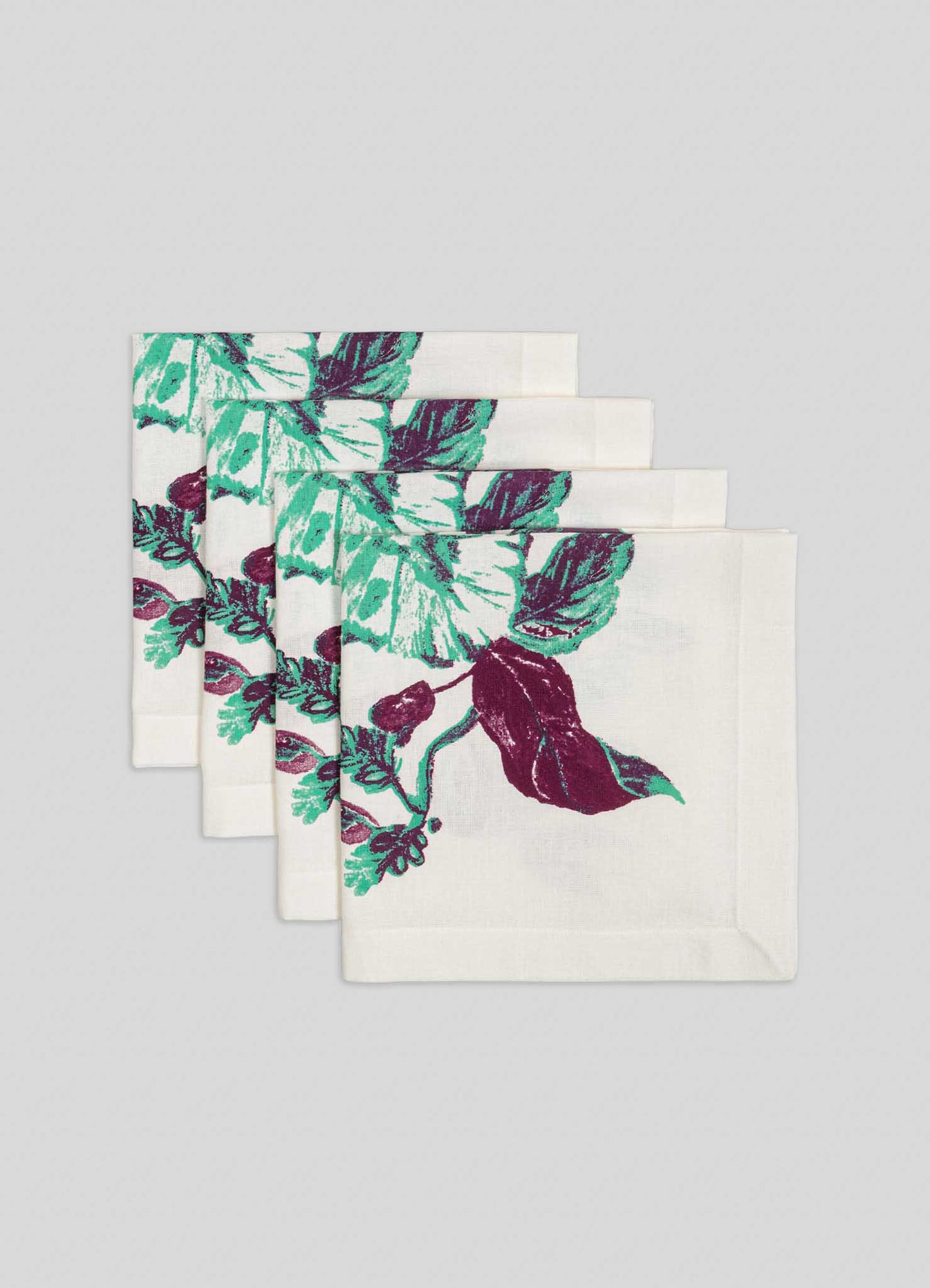 The Viya Jackfruit Green Napkins – Set of 4 features bold green and purple floral leaf designs, inspired by Indian orchards, neatly stacked against a plain light gray background.