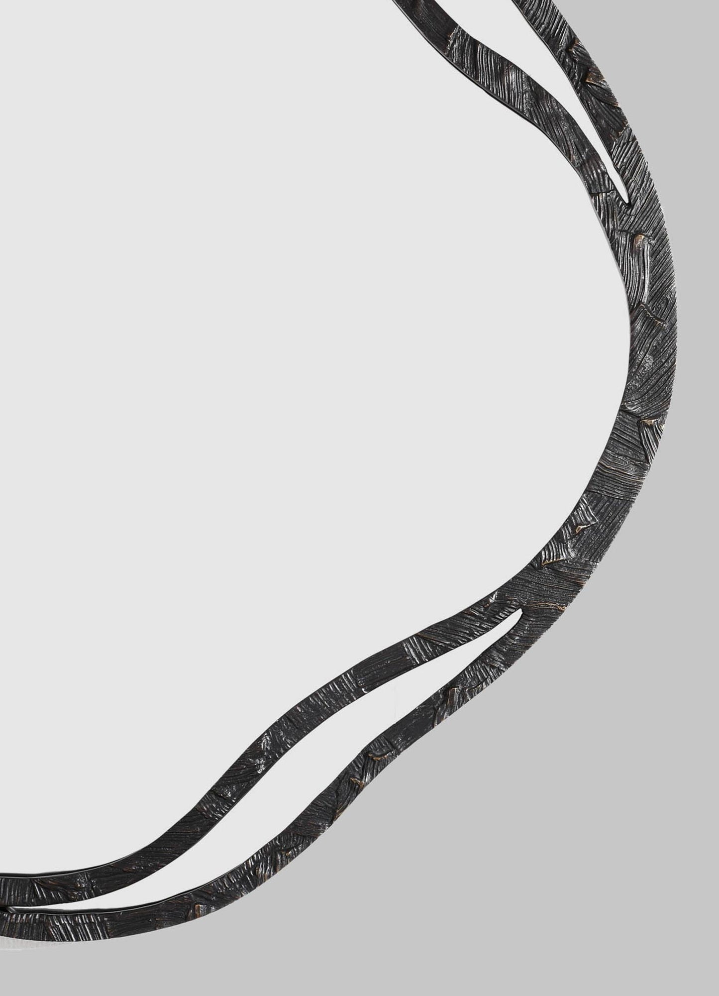 The VIYA Kolam Bronze Mirror Round Large features a curved, black textured metal frame with organic lines inspired by Indian Kolam patterns, partially surrounding a clear round mirror against a plain gray background.