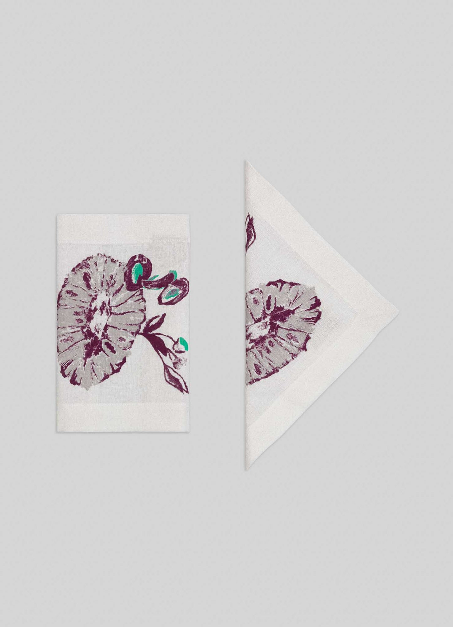 The Viya Orchard Green Cocktail Napkins (set of 4) feature a purple and teal floral mushroom pattern inspired by exotic Indian pomegranate motifs, shown folded in rectangle and triangle shapes on a light gray background.