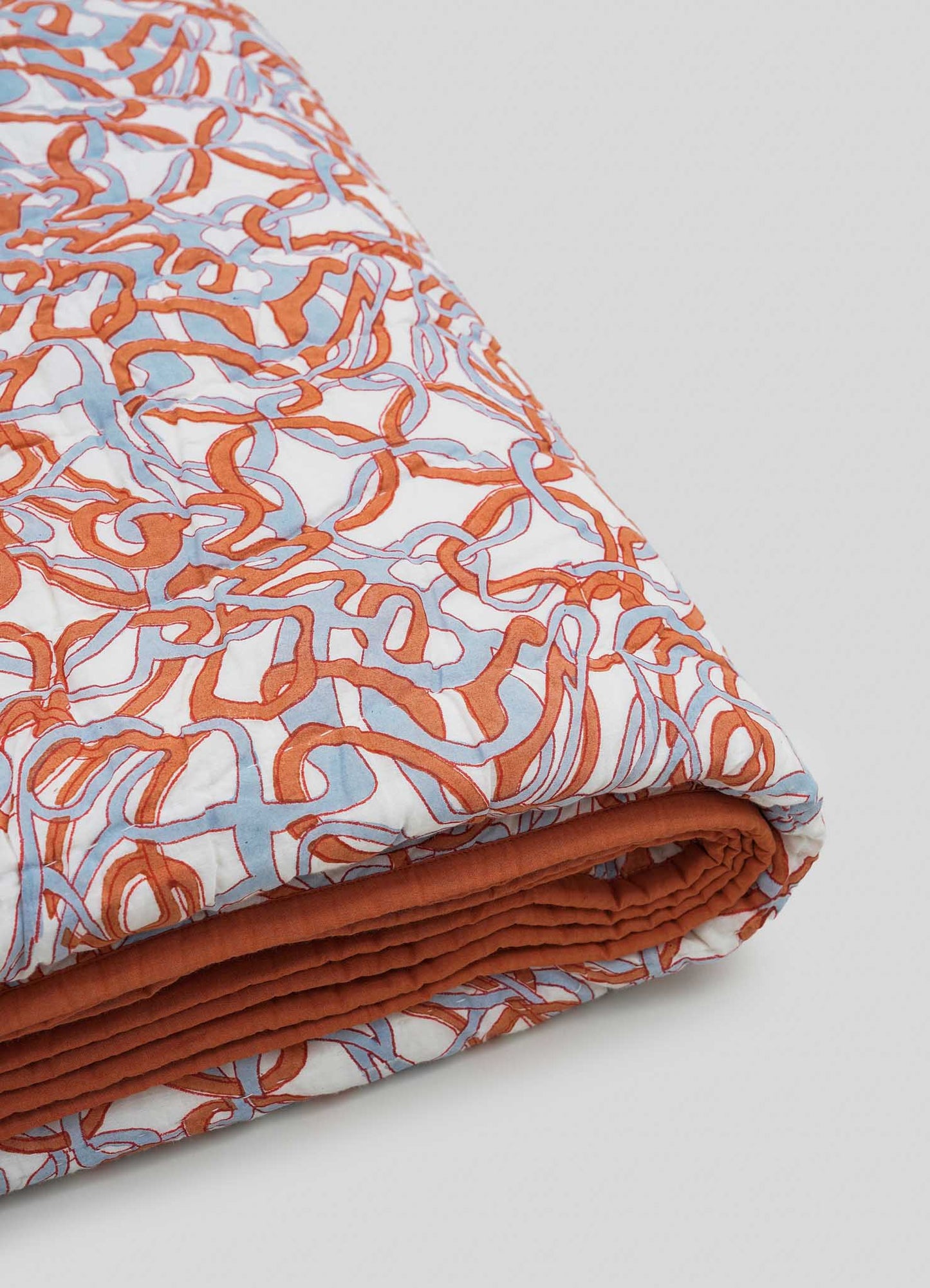 The Viya Paigah Orange & Blue Single Quilt features an abstract orange and blue pattern on white, inspired by intricate latticework, with a solid rust-colored underside.