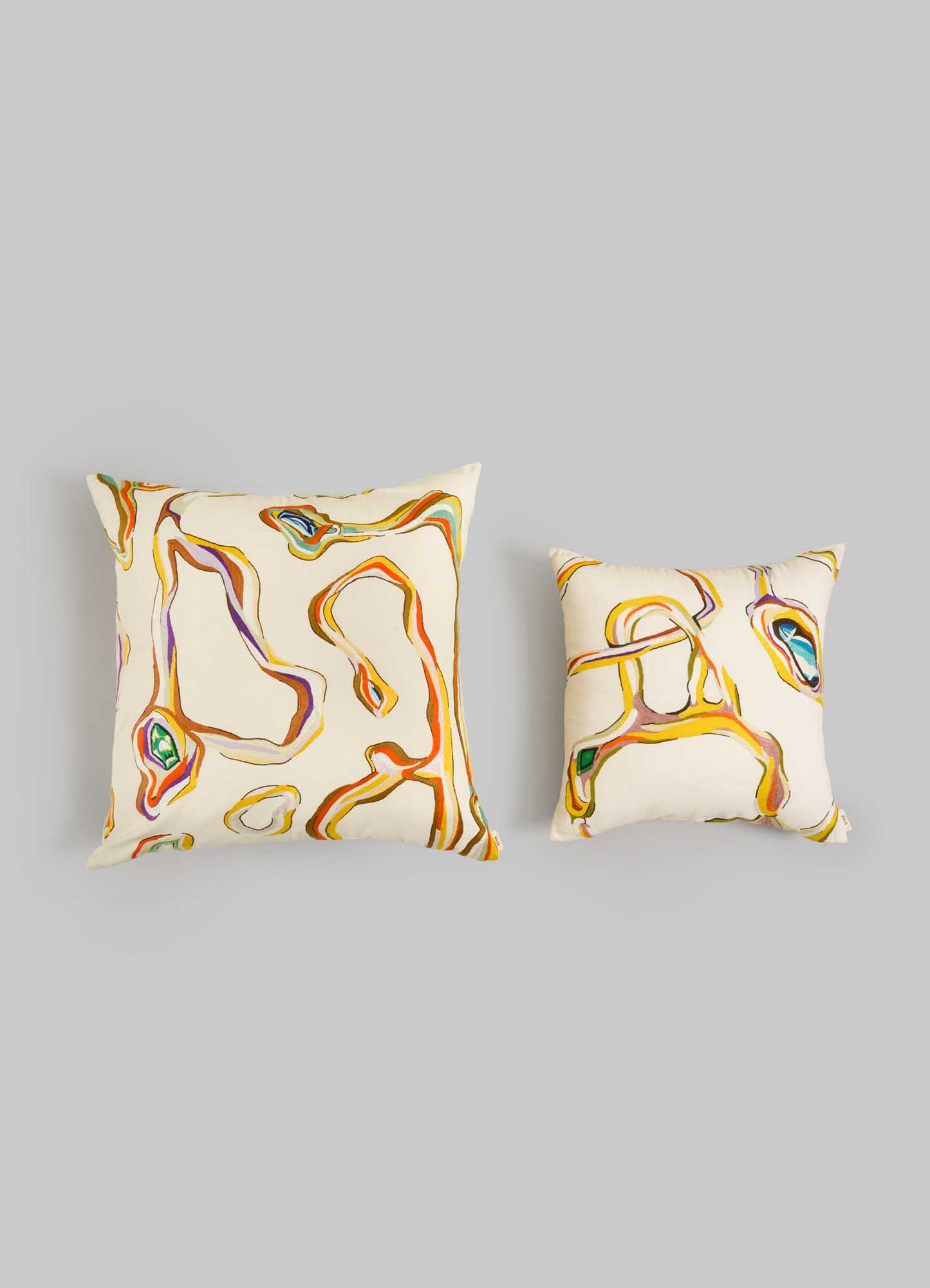 The Viya Tutti Frutti Hand Embroidered Multicolour Cushion Cover (24"x24") features abstract swirling lines in orange, yellow, brown, purple, and green on cream—perfect for modern table settings. Displayed on a light gray background.