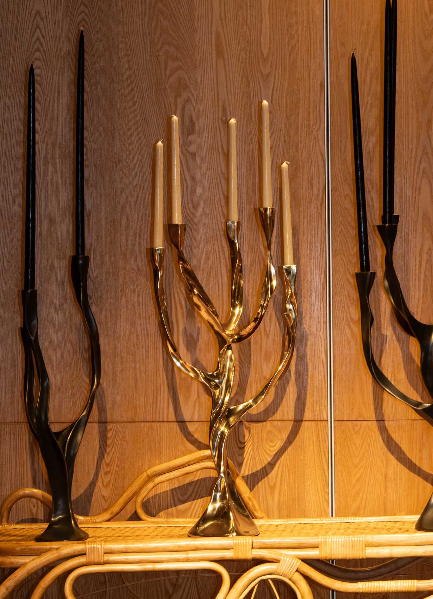 Brass candelabra with a polished gold finish holding tall, tapered candles, featuring an organic, twisting design, set against a wooden background.
