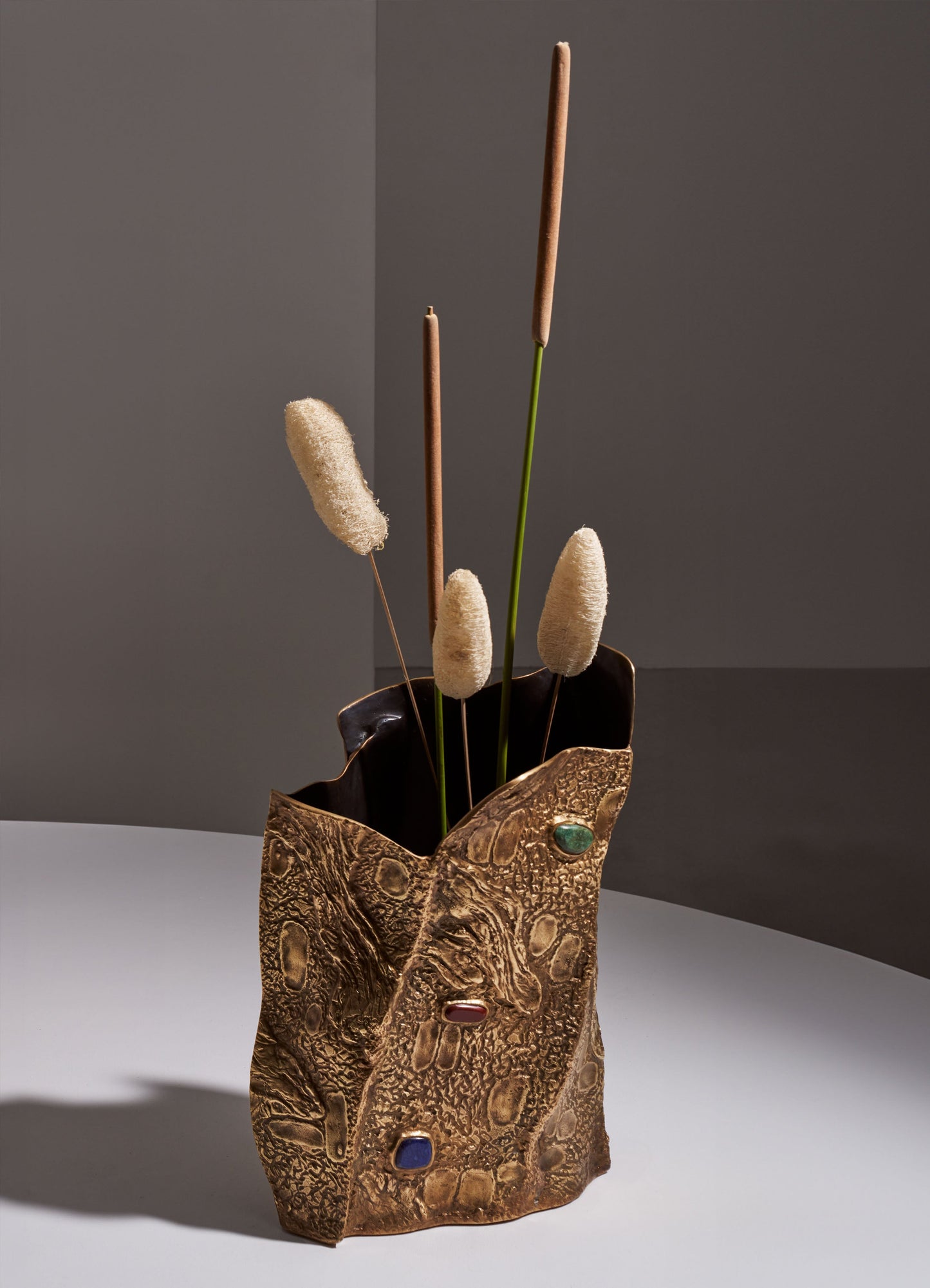 Decorative vase with a textured, gold-toned surface and embedded multicolored stones, filled with dried grasses in neutral and pastel shades.