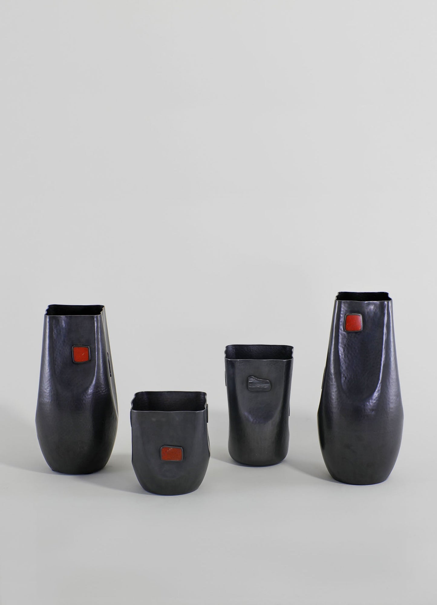 Set of four black ceramic vases with a matte finish, featuring small rectangular red accents and varying heights, on a plain light background.