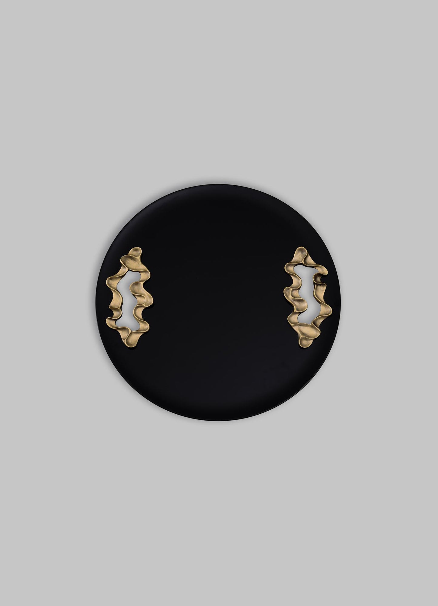 A black round tray with gold, abstract-shaped handles, made of metal, has a contemporary style with a smooth matte finish.