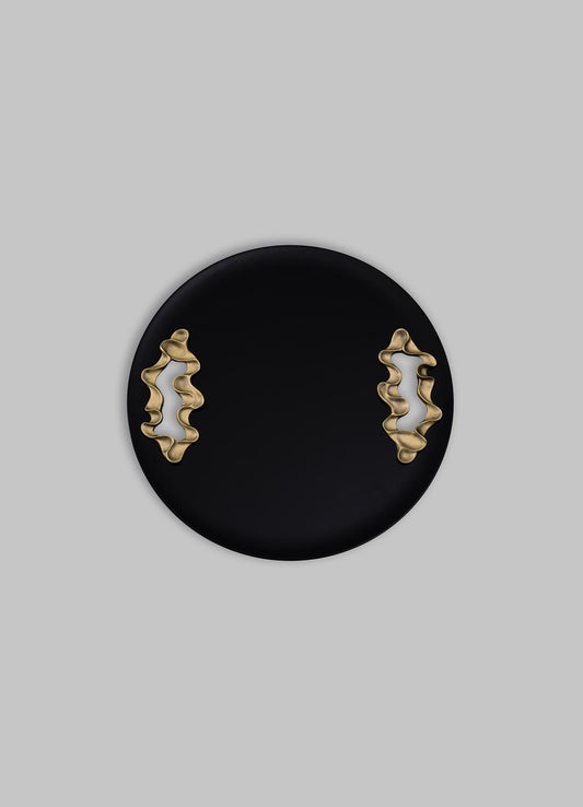 A black round tray with gold, abstract-shaped handles, made of metal, has a contemporary style with a smooth matte finish.