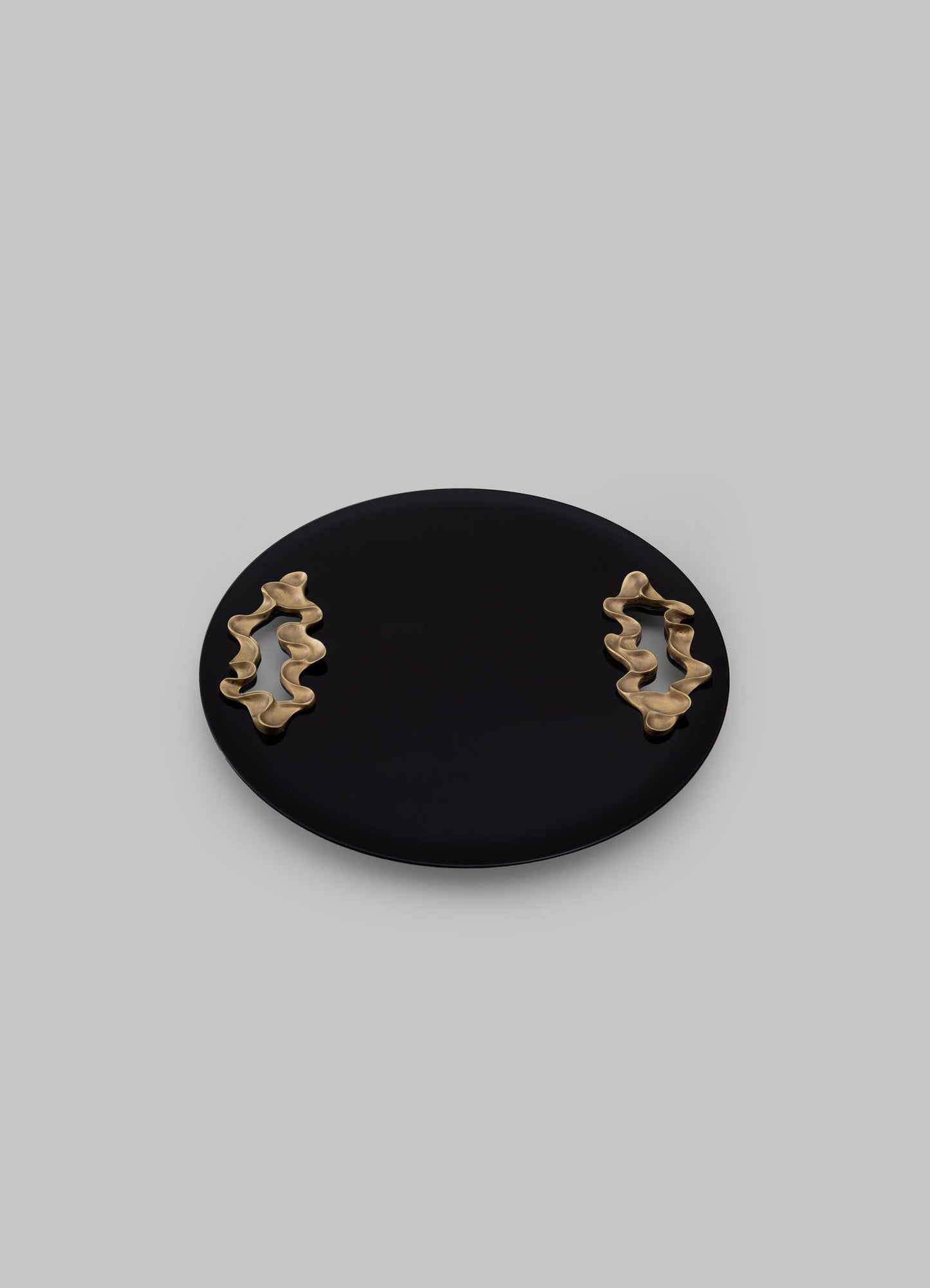 A black oval ceramic tray with two gold-toned abstract sculptural handles featuring wavy, organic shapes, set against a light gray background.