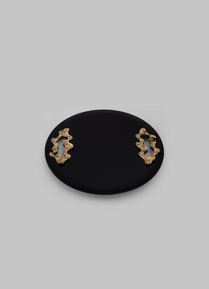 A black oval ceramic tray with two gold-toned abstract sculptural handles featuring wavy, organic shapes, set against a light gray background.