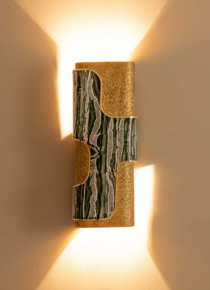 Wall sconce with a cylindrical shape featuring a combination of green and white marble and gold textured metal accents, emitting warm light that creates a glow on the wall.
