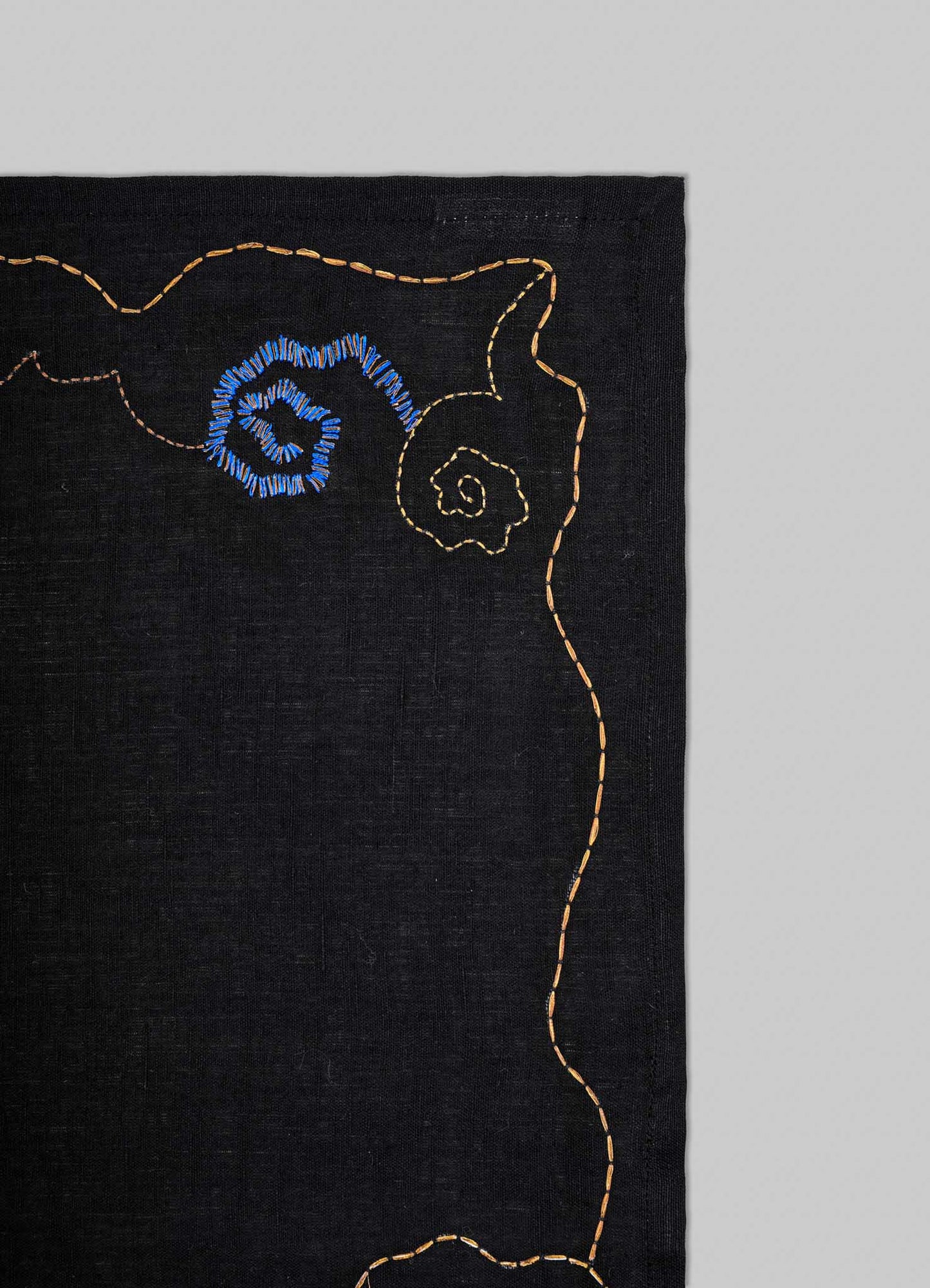 Black fabric with embroidered blue flower design on a gray background viya luxury placemats