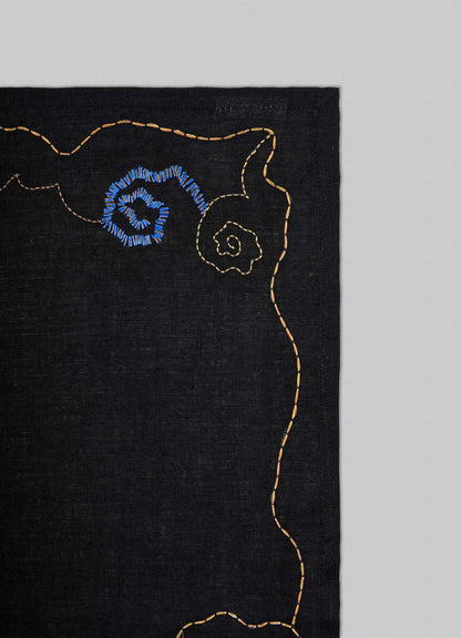 Black fabric with embroidered blue flower design on a gray background viya luxury placemats