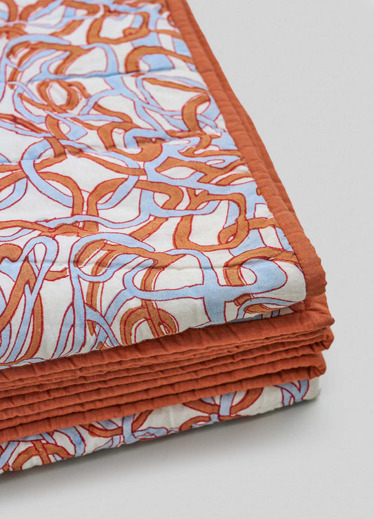 Cotton quilt with a geometric pattern in orange and light blue, edged with a solid orange border, featuring quilted stitching for texture.