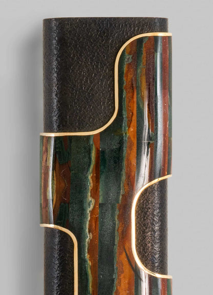 Decorative cylindrical sculpture combining textured black material with colorful, marble-like inlays in shades of green, orange, and brown, accented with gold trim. The style is contemporary with abstract geometric motifs, creating a striking visual contrast.