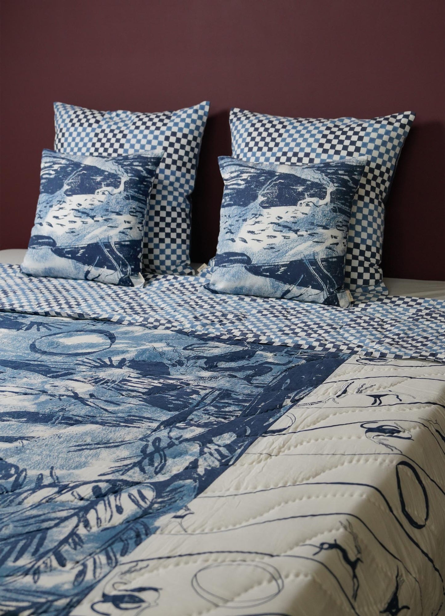 Bed with blue and white patterned bedding and pillows covers against a dark purple wall luxury cotton quilts viya