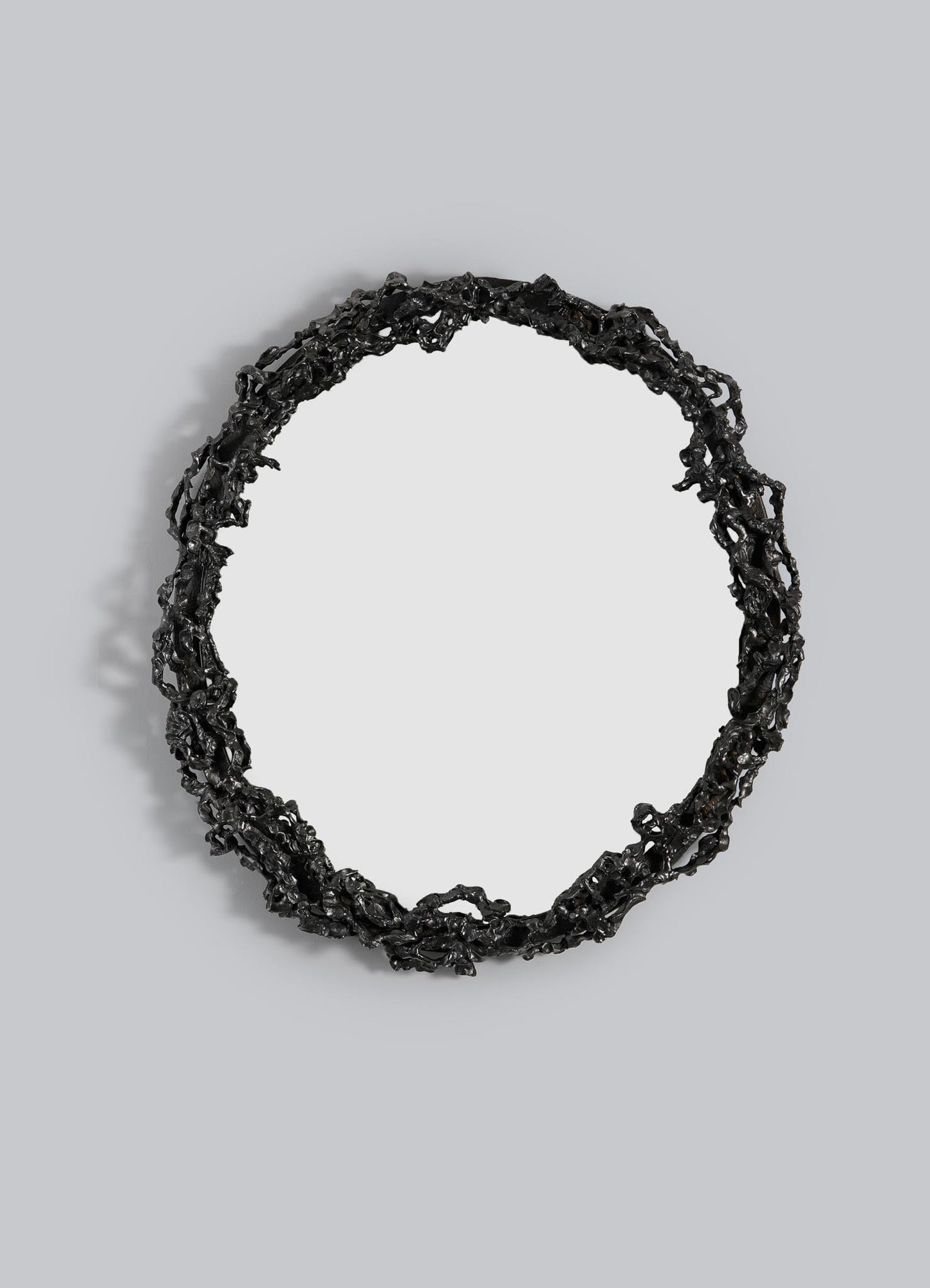The VIYA Andaman Mirror features a round design with an intricate, irregular black metal frame inspired by organic vines and branches, mounted against a plain light gray background.