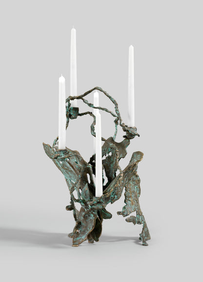The VIYA Butterfly Candle Stand Large features an abstract, organic bronze design with a weathered greenish patina, holding four tall white taper candles against a plain gray background.