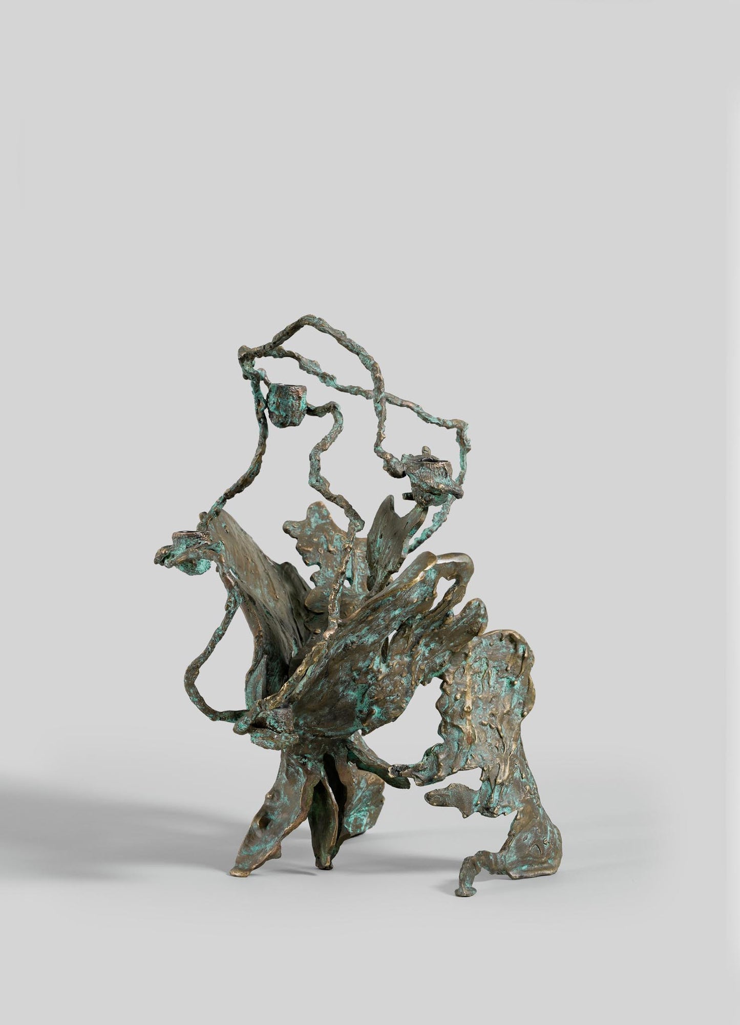 The VIYA Butterfly Candle Stand Large features an abstract bronze design with twisting, branch-like forms, a patina finish, and textured surfaces, presented against a plain gray background.