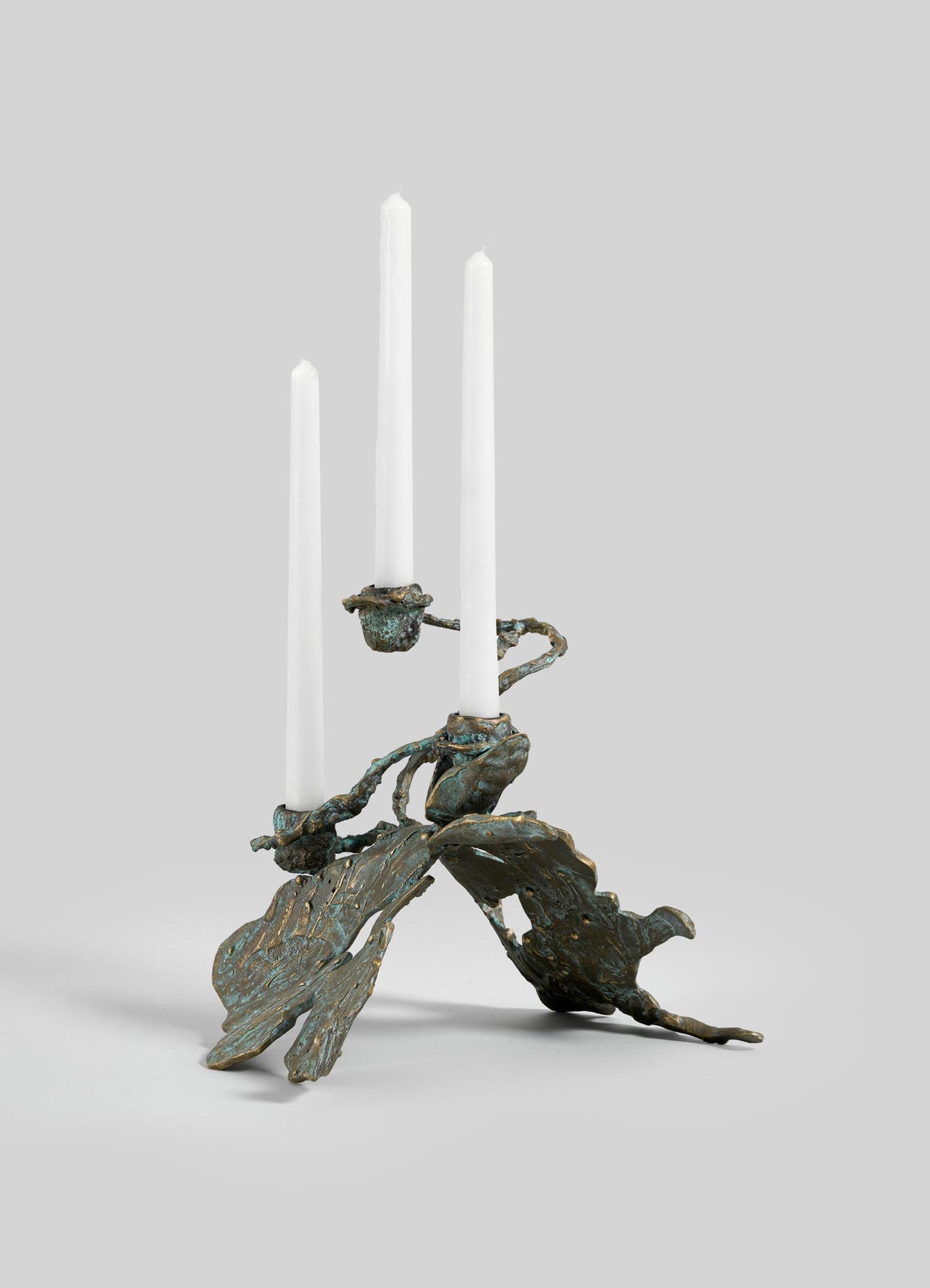 The VIYA Butterfly Candle Stand Small is a sculptural bronze candelabrum with three white candles and abstract, textured leaf-shaped arms and base, displayed against a plain light gray background.