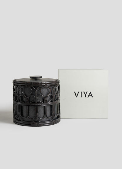 A dark, ornately carved cylindrical Manipur Ice Bucket Large by VIYA sits beside a plain, light-colored VIYA box and elegant barware accessories, all set against a neutral background.