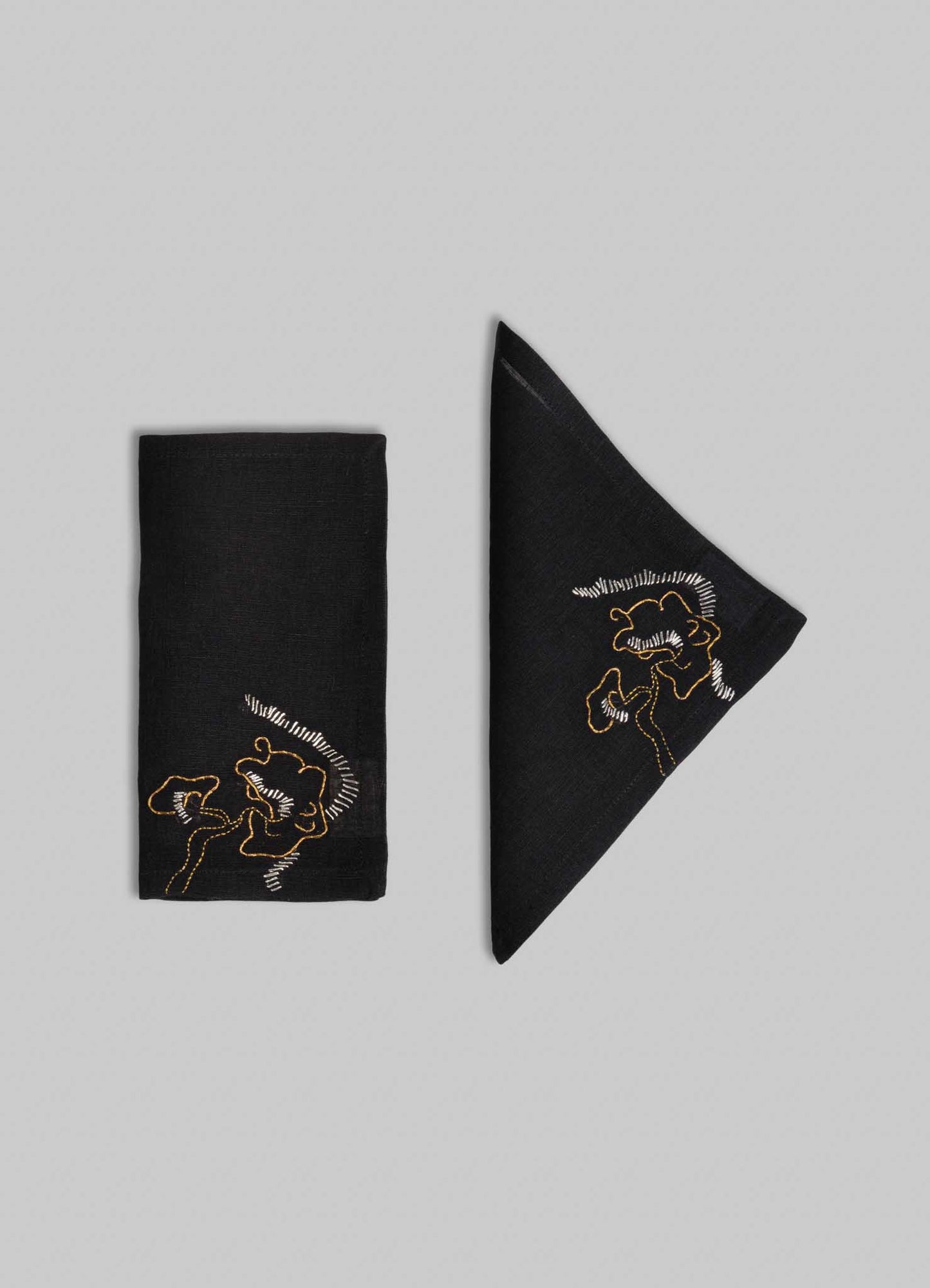 Viya Blackbuck Dreams Hand Embroidered Black & Gold Cocktail Napkins, Set of 4—black napkins featuring abstract face designs in yellow and white thread on a light grey background.