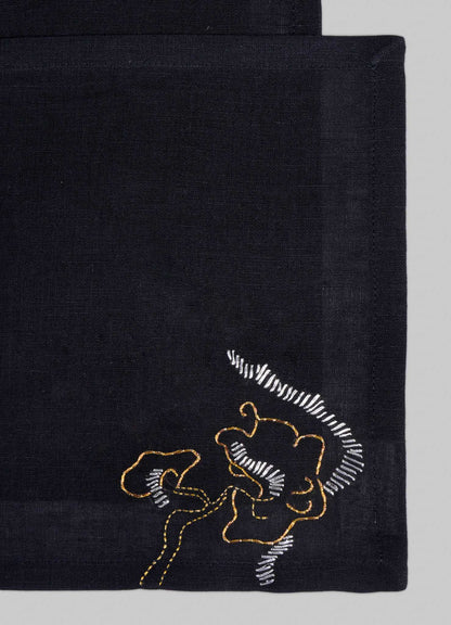 The Viya Blackbuck Dreams Hand Embroidered Black & Gold Cocktail Napkins (Set of 4) feature abstract face motifs in yellow and white thread on black fabric, inspired by Indian manuscripts.