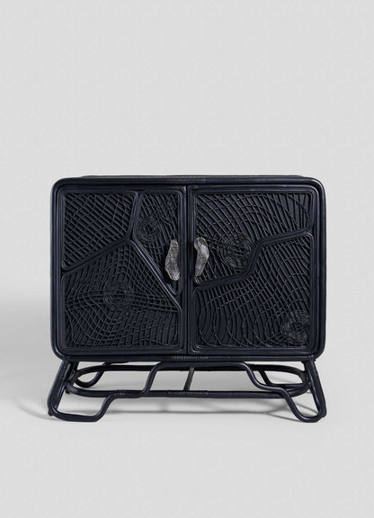 The VIYA Chakra Cabinet features two front doors with geometric cane weaving, curved legs, and two clear handles, all in black rattan, set against a plain light gray background.