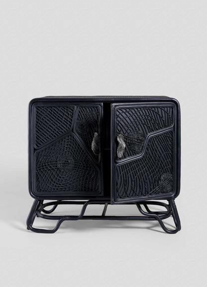 The VIYA Chakra Cabinet is a black rattan cabinet with two doors and geometric cane patterns, set on a matching frame, shown against a plain light gray background.