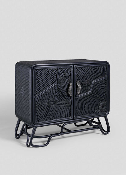 The Chakra Cabinet by VIYA features intricate cane-weaved black doors and a tubular metal base, presented against a plain light gray background.