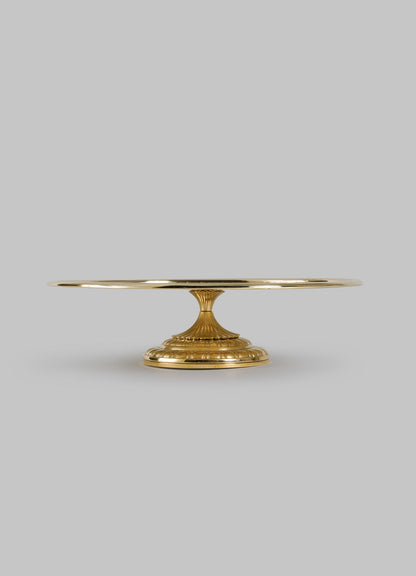 The City Palace Cake Platter by VIYA features a round, flat top and ornate pedestal base, inspired by handcrafted Jaipur brass decor, displayed against a plain light gray background.