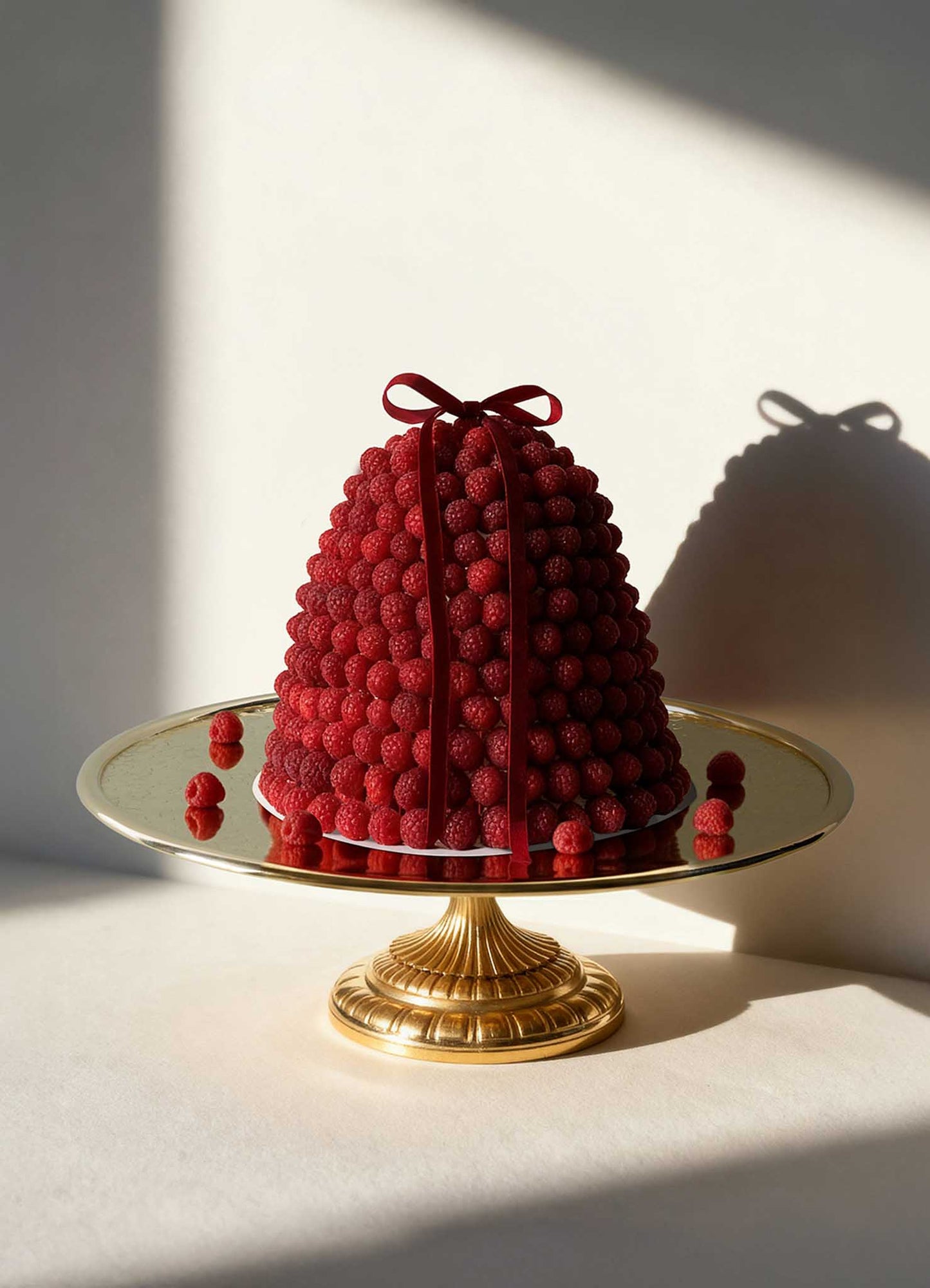 A dome-shaped cake crowned with fresh raspberries and a red ribbon rests on the VIYA City Palace Cake Platter. Handcrafted cast brass candelabras from Jaipur in Bloom add elegance, with raspberries scattered at the base.