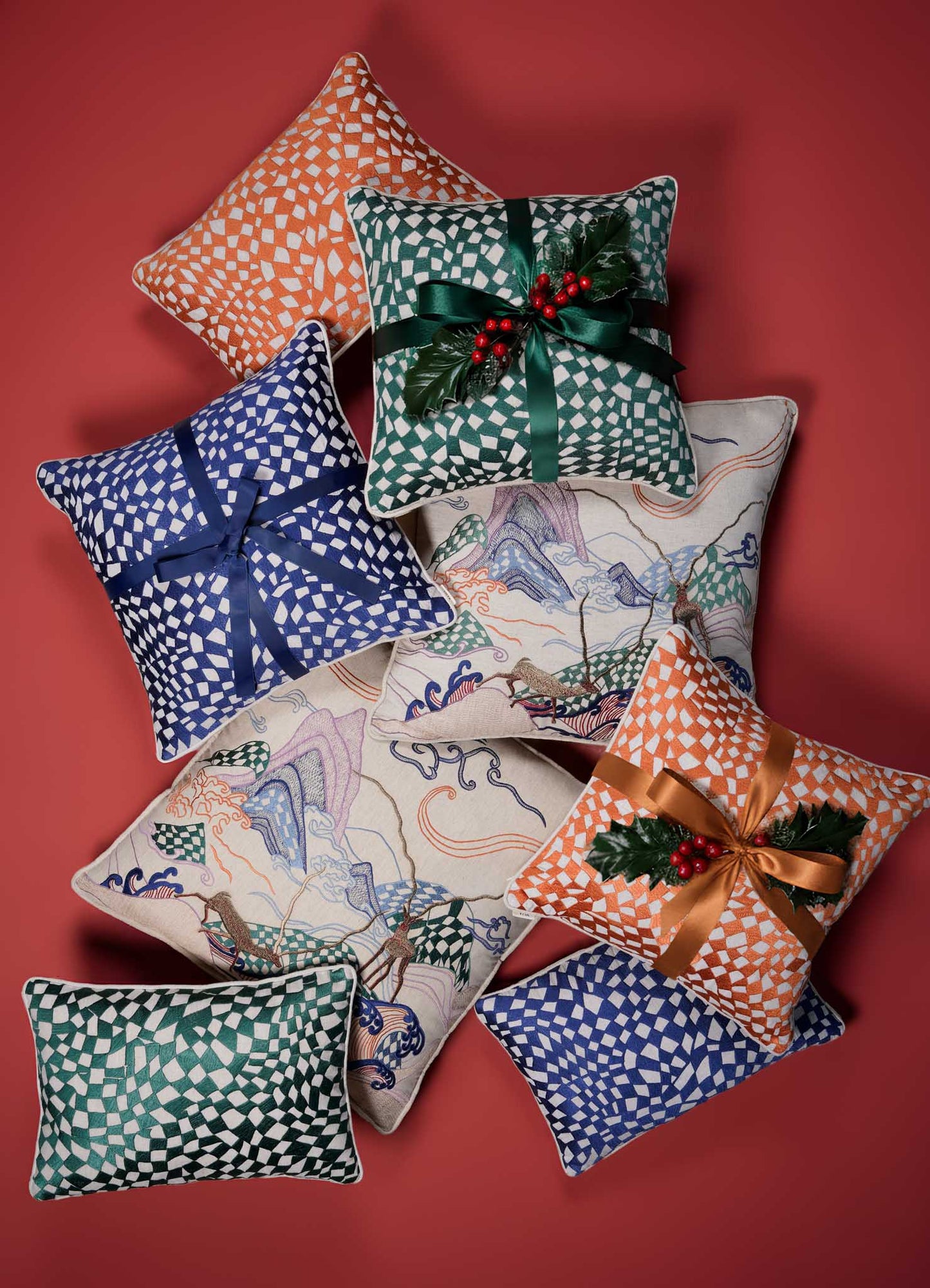 The Dreamscape Orange Embroidered Checks Cushion Cover 12"x18" by Viya is arranged with other festive pillows on a red background. It features a nature-inspired orange check motif, perfect for holiday décor.