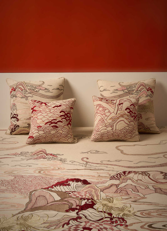 Four Viya Dreamscape Red Embroidered Cushion Covers (24"x24") featuring intricate wave and mountain motifs in beige, red, brown, and cream are arranged against a muted wall with a matching carpet and a bold burnt orange background.