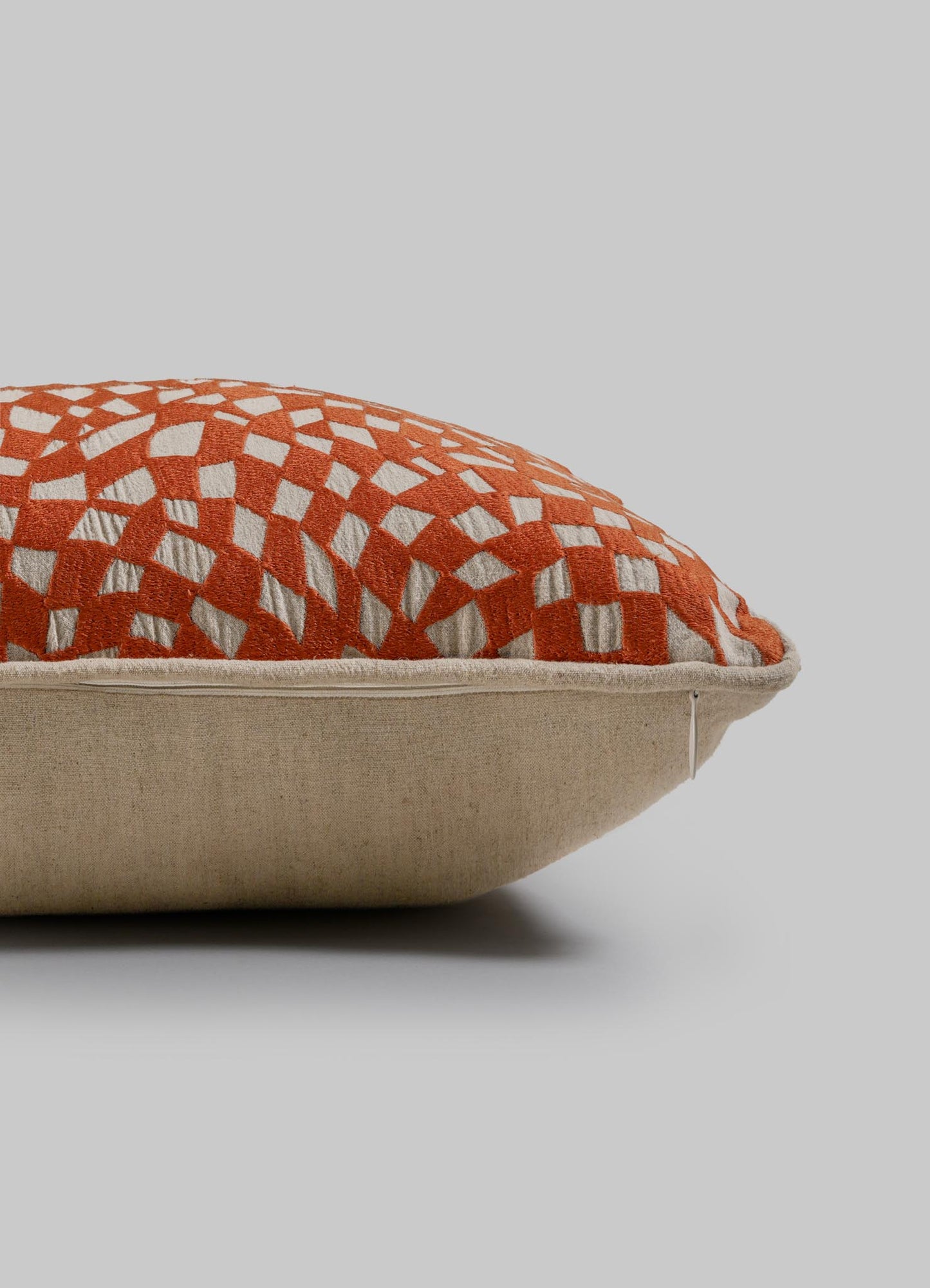 The Viya Dreamscape Orange Embroidered Checks Cushion Cover (12"x18") features a beige base, orange top, and white geometric diamond pattern inspired by embroidered textiles. Shown against a plain light gray background.