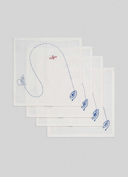 A set of four ecru hand-embroidered face towels by Viya, inspired by the Evil Eye motif, are stacked on a light gray background. Blue embroidery and unique designs decorate each towel in this protective Nazar-themed set.
