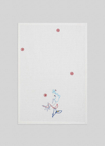 The Viya Evil Eye Hand Embroidered Ecru Hand Towels (Set of 2) feature a white textured finish with small red target-like Nazar motifs and a blue and red abstract line art figure near the bottom, set against a light gray background.