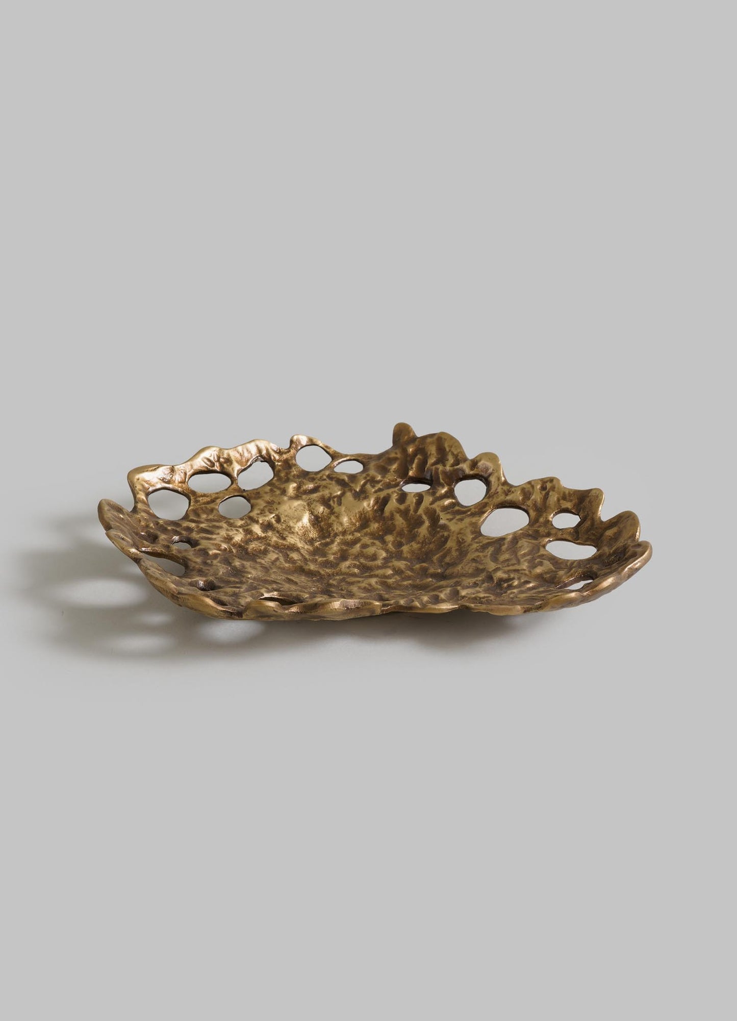 The VIYA Golden Coral Bowl features an irregular brass design with a textured surface and open edge holes, displayed against a plain gray background.