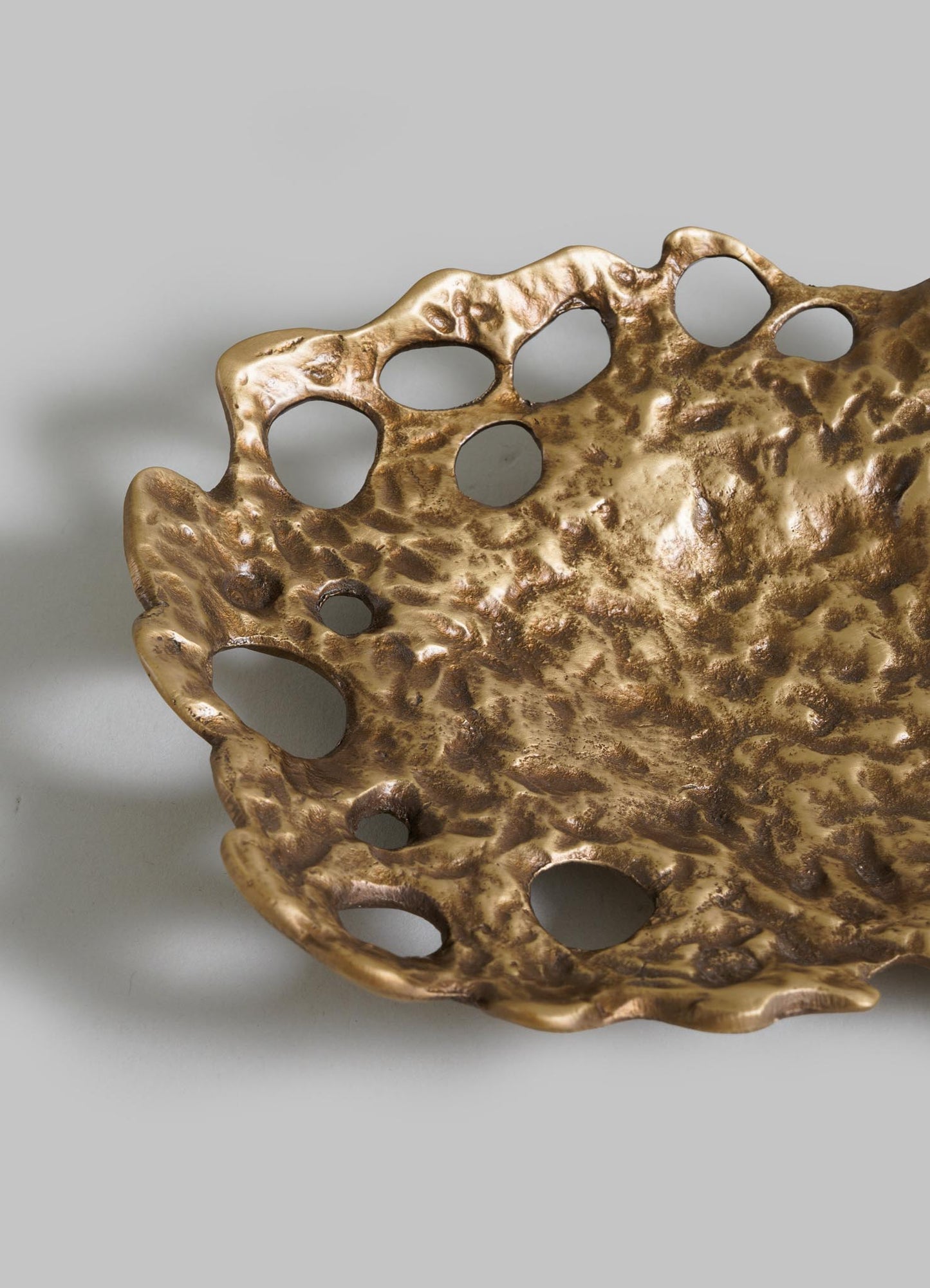Close-up of the VIYA Golden Coral Bowl, a decorative metallic piece with an organic, textured design and large holes along the ruffled edge. It has a gold finish and is displayed on a plain light background.