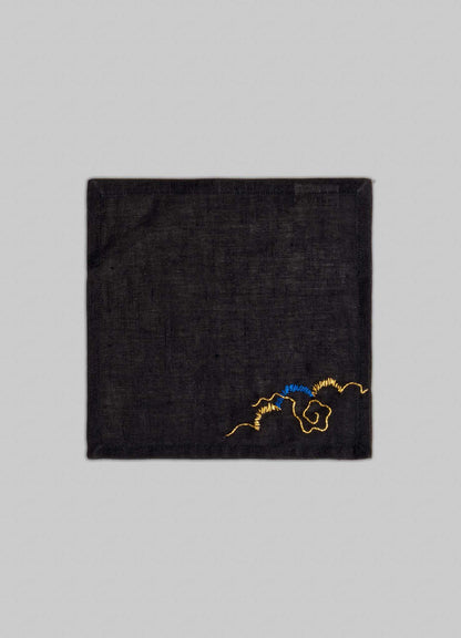 The Viya Gajasimha Hand Embroidered Black & Gold Cocktail Napkins, set of 4, feature small gold and blue floral embroidery in one corner, inspired by the mythical guardian from ancient Indian art. Set against a plain light gray background.