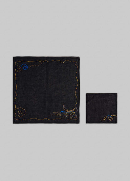 The Viya Gajasimha Hand Embroidered Black & Gold Napkin features gold and blue designs, including a mythical Indian Gajasimha, shown both fully open and neatly folded on a light gray background.