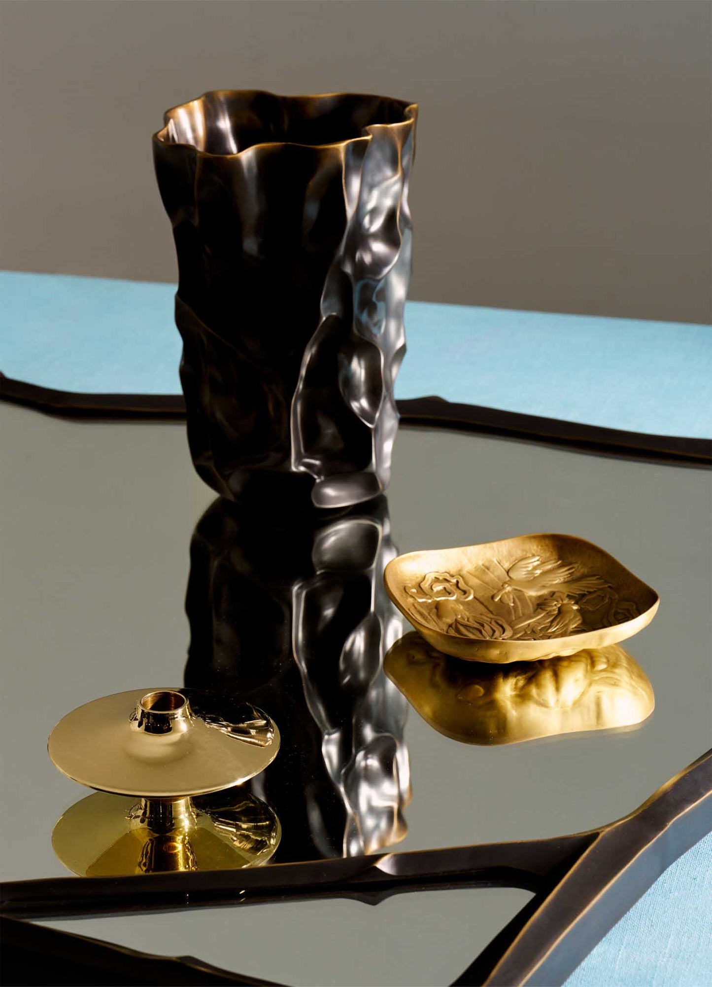 The VIYA Himalaya Vase Large stands alongside a gold engraved tray and candle holder on a reflective surface, evoking the Himalayan range’s serenity, with a blue accent in the background.