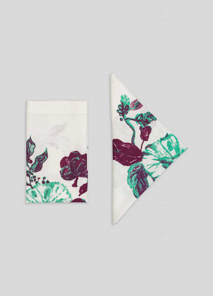 Two Jackfruit Green Napkins from Viya, inspired by Indian fruit orchards, feature green and burgundy florals; one is folded into a rectangle, the other into a triangle, both displayed on a light gray background.