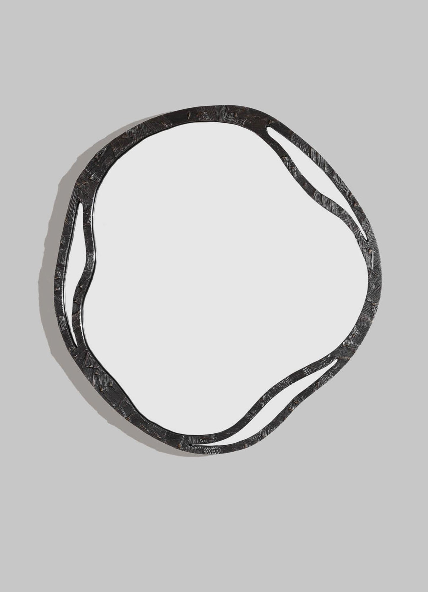 The VIYA Kolam Bronze Mirror Round Large features an irregular, organic-shaped black metal frame that captures the artistry of Indian decor, displayed against a plain light gray background.