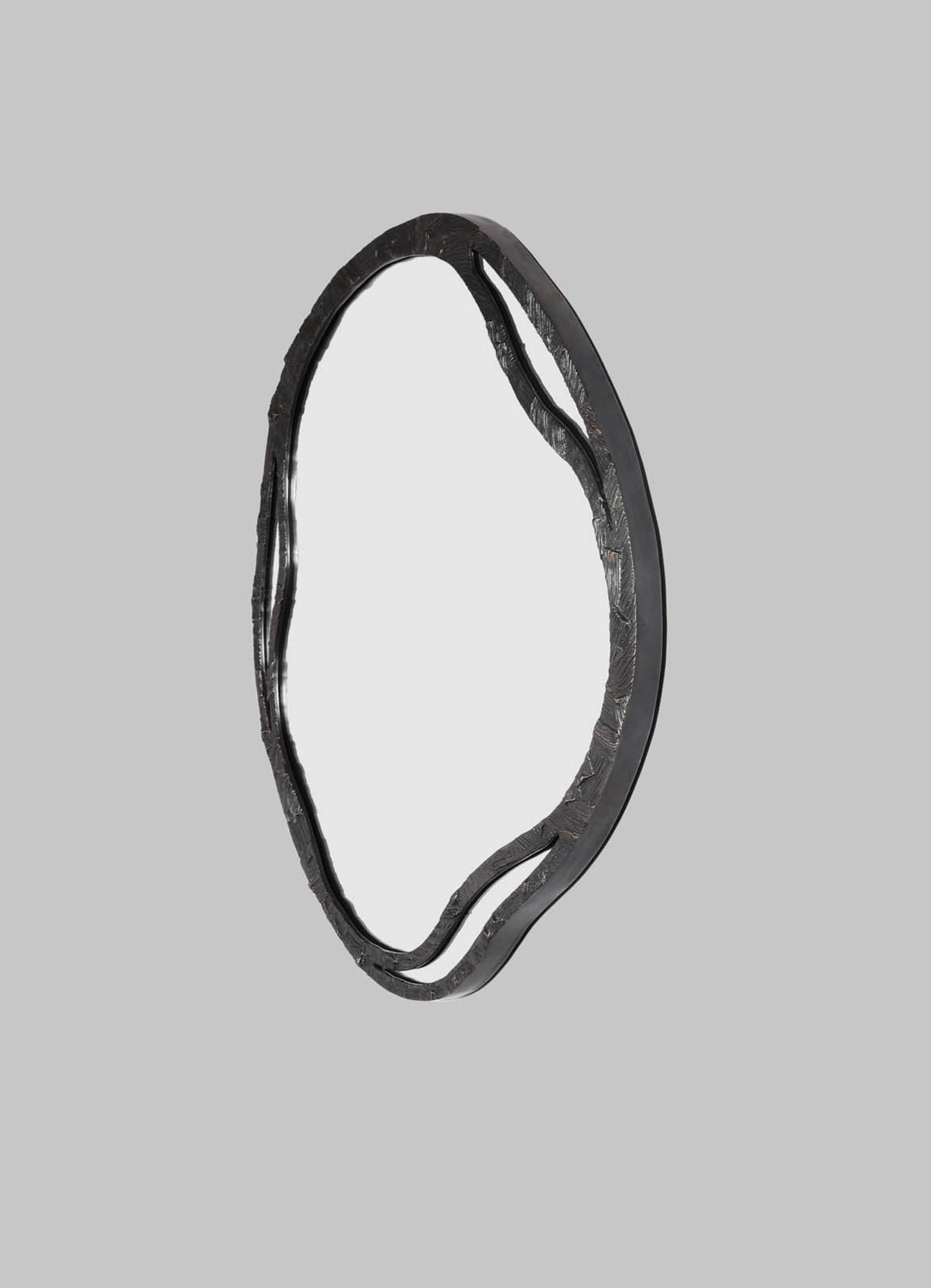 The VIYA Kolam Bronze Mirror Round Large features an artistic, irregular sculpted metal frame with wavy edges, inspired by Indian Kolam patterns. Shown against a plain gray background.