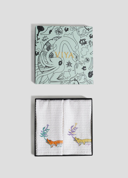 The Lurking Crocodile Hand Towels by Viya come as a set of 2, packaged in a decorative black box with "Viya" in gold, featuring folded white towels embroidered with vibrant aquatic animals and plants.